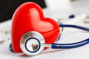 A stethoscope surrounds a heart resting on top of medical notes.