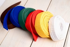 Several martial arts belts of all different colors are stacked in order on a wooden table.