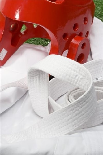 A red sparring helmet rests on a clean white martial arts uniform.