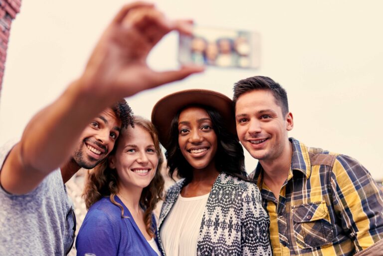 Multi-ethnic millenial group of friends taking a selfie photo with mobile phone on rooftop terrasse at sunset