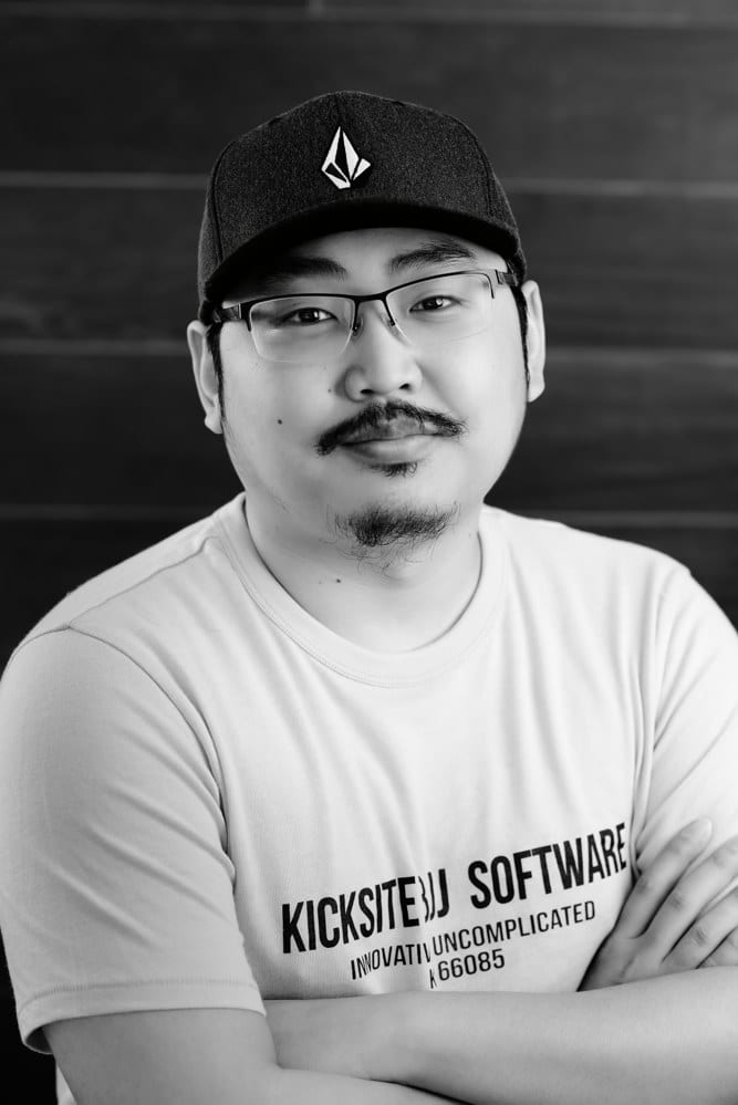 Man with hat and glasses standing against brick backdrop