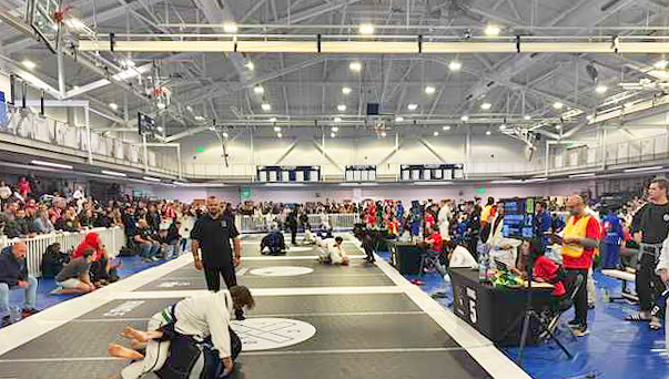 A Jiu-Jitsu event with grapplers on mats and crowds watching