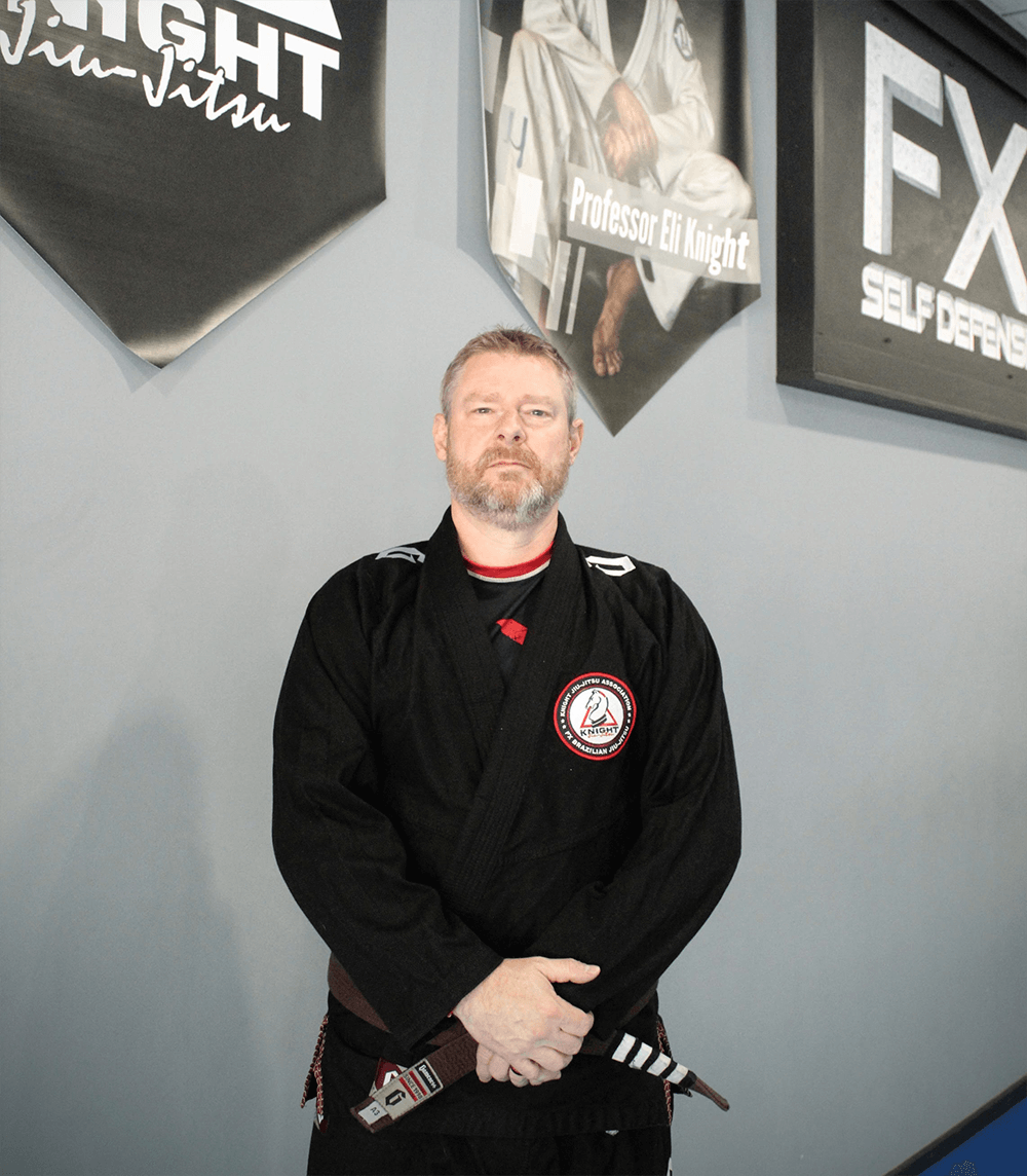 Rocky Frizzell wearing a gi and standing in front of an FX Self Defense banner